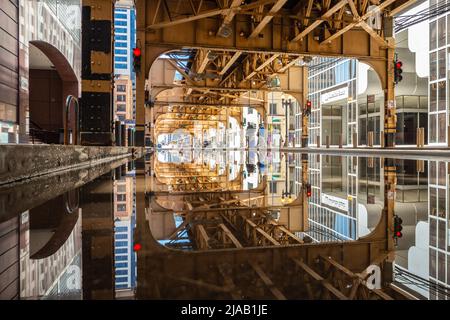 Die Oberleitungen an der West Van Buren Street, Chicago, spiegeln sich in einer großen Pfütze auf der Straße wider. IL, USA, Reise, Straße, abstrakt. Unter dem El Stockfoto