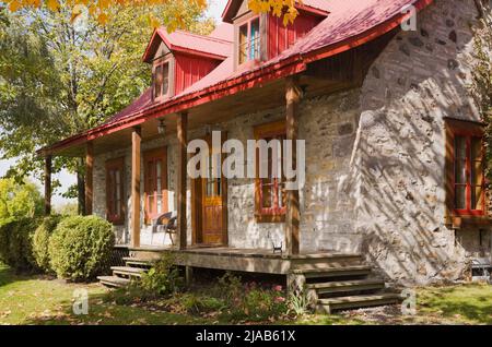 Alte, um 1786 im kanadischen Cottage-Stil erbaute Feldsteinhaus-Fassade mit rotem Blechdach im Herbst. Stockfoto