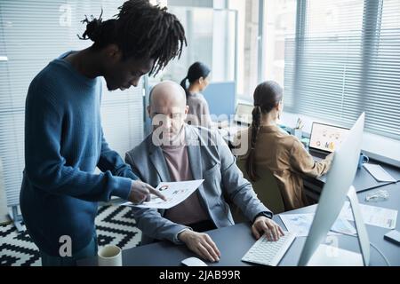 Porträt eines reifen Geschäftsführers, der junge Mitarbeiter im Büro berät und Datendiagramme und Kopierflächen ansieht Stockfoto