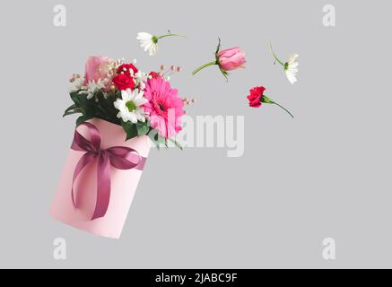 Rosa Geschenkbox mit verschiedenen Blumen auf grauem Hintergrund. Fliegende Blumen aus der Schachtel. Valentinstag ästhetische Natur Konzept. 8 März Karte Idee. Stockfoto