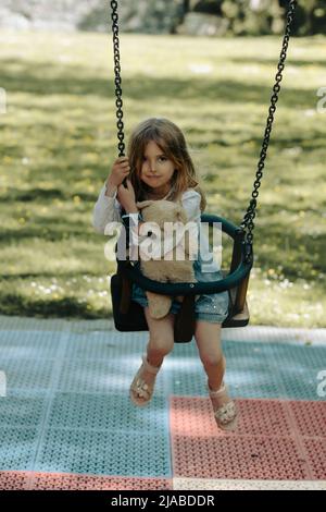 Das 5-jährige Mädchen spielt im Park, während es ihren Teddybären hält Stockfoto