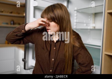 Die junge Frau schließt ihre Nase wegen des unangenehmen Geruchs aus dem Kühlschrank Stockfoto