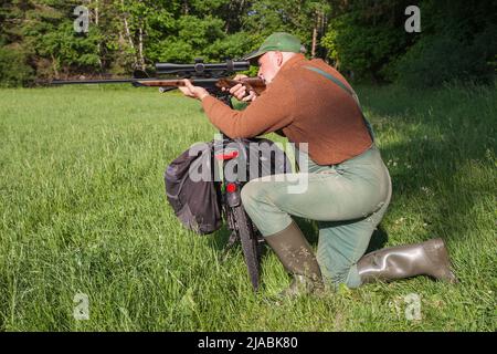 Umweltbewusster, ökologischer Jäger, der mit seinem Fahrrad umweltfreundlich auf die Jagd ging und es jetzt als Gewehrkissen nutzt. Stockfoto