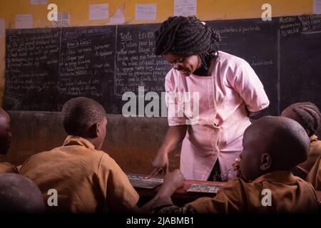 Schwarzer Lehrer, der sehr aufmerksamen Schülern das Schreiben auf der schwarzen Tafel erklären will. Stockfoto