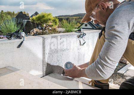 Kaukasischer Landschaftsbau-Techniker in seinem 40s Installation von Outdoor-Gartenbeleuchtung entlang Beton Hinterhof Treppe. Landschaftsbau. Stockfoto