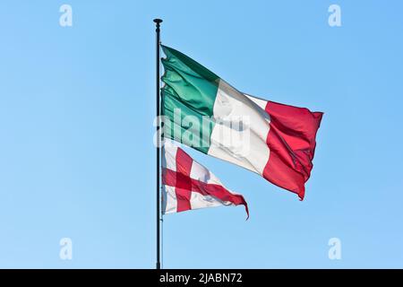 Nationalflagge Italiens und Flagge Genuas, Hauptstadt der italienischen Region Ligurien, winken im Wind vor klarem blauen Himmel Hintergrund Stockfoto