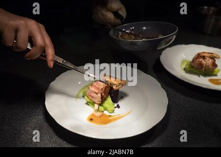 Chef Koch setzen gegrilltes Fleischstück mit einer Pinzette auf grünes Gemüse püriert weißen Teller mit Sauce. Gesunde Mahlzeiten Zubereitung, Kochen oder Kleinbus Stockfoto