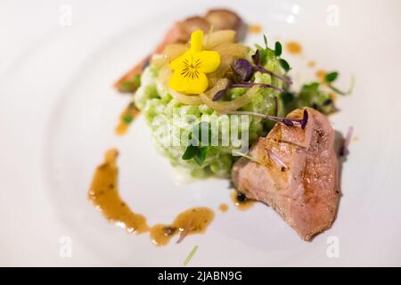 Gegrilltes Fleischstück auf dem weißen Teller serviert mit grünen Erbsen mit Sahnesauce und Microgreens. Gesunde Mahlzeiten Zubereitung und Kochen Konzept Stockfoto