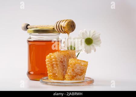 Honig Hintergrund. Süßer Honig im Kamm. Frischer Honig im Glas, Waben, Honiglöffel und weiße Blumen auf hellem Hintergrund. Stockfoto