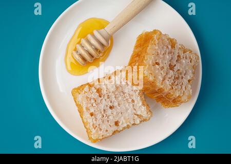 Honig Hintergrund. Süßer Honig im Kamm. Waben und Honiglöffel mit Honig in einer weißen Keramikplatte. Draufsicht. Stockfoto