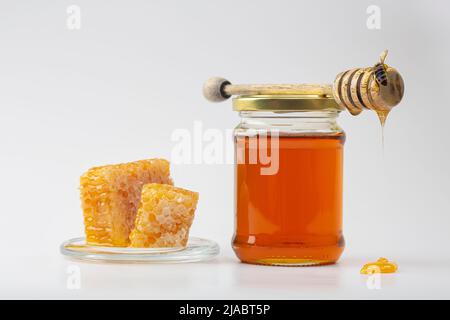 Honig Hintergrund. Süßer Honig im Kamm. Frischer Honig im Glas, Waben, ein Löffel für Honig und eine Biene auf hellem Hintergrund. Stockfoto