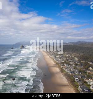 Aus der Luft schießen. Majestätischer Ozean, sandige Küste und eine kleine grüne Stadt am Wasser. In der Ferne ist eine Bergkette sichtbar. Hellblau Stockfoto