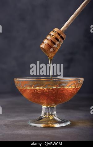 Honig Hintergrund. Honig tropft aus einem Dipper in einer Glasschüssel. Nahaufnahme. Gesunder Bio-dicker Honig, der aus dem hölzernen Honiglöffel taucht, aus der Nähe Stockfoto