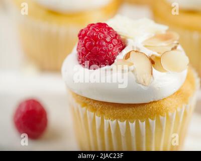 Makrofotografie. Appetitliche Muffins mit Rahm, frischen Himbeeren und Mandeln auf weißem Hintergrund. Süßes Essen, Kalorien. Einladung für einen Urlaub, Stockfoto