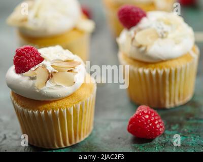 Helles, gesundes Dessert - Muffins mit Rahm, Himbeeren und Nüssen auf dunklem Marmorboden. Nahaufnahme. Auf dem Foto befinden sich keine Personen. Geburtstag, ein Stockfoto