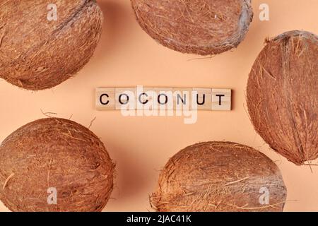 Fünf braune Kokosnüsse und Inschrift Kokosnuss aus Holzwürfeln. Flache Lay-Komposition. Stockfoto