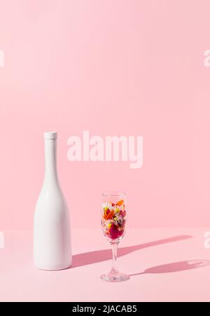 Champagner-Flasche und Glas gefüllt mit Frühlingsblumen auf rosa Hintergrund. Elegante Komposition zur Feier. Stockfoto