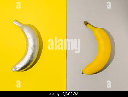 Zwei farbige bemalte Bananen auf gelbem und silbernem Hintergrund. Modernes sommerliches Fruchtkonzept. Flach liegend. Stockfoto