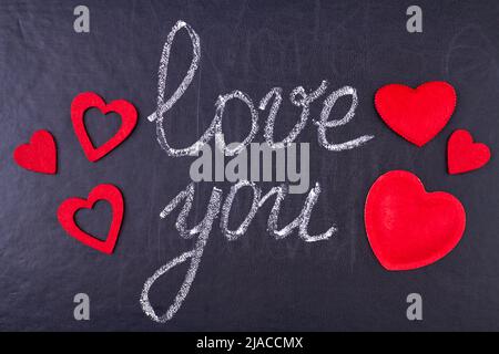 Handgeschriebene Kreidebeschriftung I love you auf schwarzer Kreidetafel mit roten Schmuckherzen. Botschaft der Liebe. Stockfoto