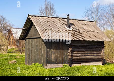 Tagsüber ein kleines russisches Saunagebäude im Außenbereich. Klassische ländliche Holzarchitektur Beispiel. Stockfoto