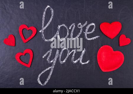 Handgeschriebene Kreidebeschriftung I love you auf schwarzer Kreidetafel mit roten Schmuckherzen. Botschaft der Liebe. Stockfoto