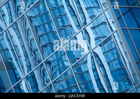 Abstrakt in Blautönen moderner Bürofenster mit verzerrter Spiegelung eines gegenüberliegenden Gebäudes mit schrägem Blickpunkt Stockfoto
