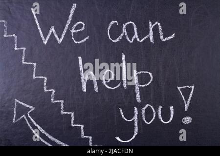 Wir können Ihnen helfen, handschriftliche Beschriftung mit weißer Kreide auf Kreidetafel. Hilfeangebot. Stockfoto