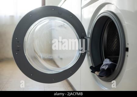 Nahaufnahme der geöffneten Tür der Waschmaschine mit der Kleidung in der Trommel Stockfoto