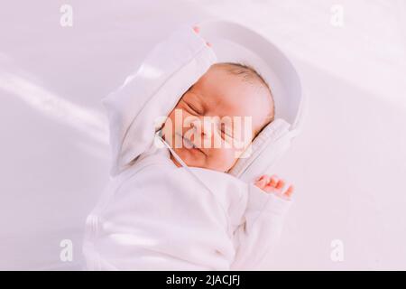 Das Kind trägt Kopfhörer. Frohes Baby. Ein neugeborenes Baby. Weiß auf Weiß Stockfoto