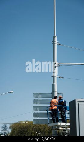 Zwei Arbeiter in einer Hubwiege an einer Laternenpfosten. Arbeit in der Höhe. Kommunale Dienste Stockfoto