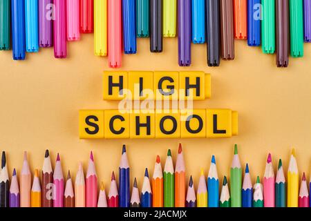 Satz von Buntstiften und Inschrift High School auf gelben Würfel. Flache Lay-Komposition. Stockfoto