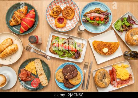 Blick von oben auf eine Reihe von Dessertplatten, Zimtrollen, Kekse, verschiedene Croissants, Salat-Sandwiches, Schokoladenchips und Eierfrühstück Stockfoto