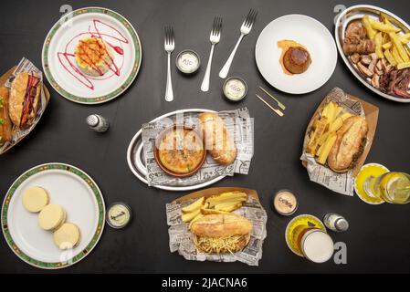 Verschiedene Teller mit Sandwiches, pommes frites, Roastbeef in Scheiben, Panna Cotta und Käsekuchen Stockfoto