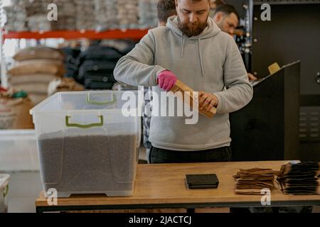 Männlicher Arbeiter packt nur geröstete Kaffeebohnen in Verpackungen zum Verkauf Stockfoto