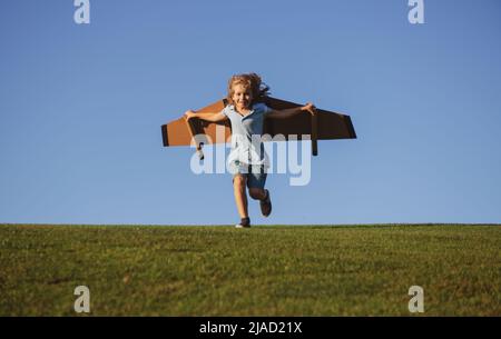 Kinderreisender mit Rucksackflügeln. Kind spielt Flieger und träumt im Park. Kleiner Junge Pilot gegen einen blauen Himmel. Stockfoto