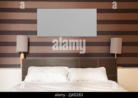 Kopfteil in einem Schlafzimmer mit Lederbezug, zwei Lampen und dekorativem Papier an der Wand Stockfoto