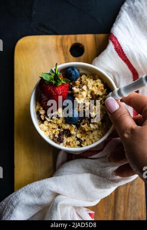 Ansicht von oben einer Frau, die nach einer Schüssel Haferflocken mit frischen Blaubeeren und Erdbeeren greift Stockfoto