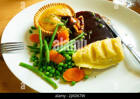 Leckere Mahlzeit Steak und Ale Pie mit Kartoffelpüree aufgeschnitten Tender Stem Brokkoli Karotten Erbsen und Soße Stockfoto