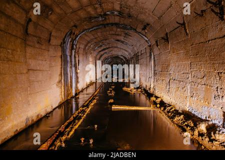 Dunkel überfluteter Beton-gewölbter Minentunnel. Stockfoto