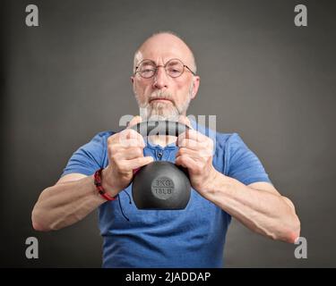 Älterer Mann (Ende 60s) trainiert mit eiserner Kettlebell, aktiver Senior und Fitnesskonzept Stockfoto