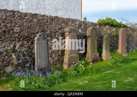 Nahaufnahme von alten Grabsteinen in einer Reihe auf einem europäischen Friedhof mit Steinmauer im Hintergrund Stockfoto