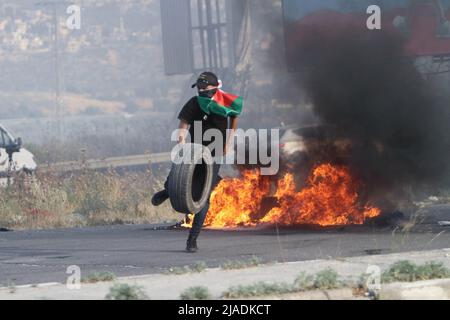 Nablus, Westjordanland, Palästina. 27.. Mai 2022. Palästinensische Demonstranten verbrennen Reifen während einer Demonstration gegen das Eindringen jüdischer Siedler in die Al-Aqsa Moschee und die Organisation des marsches israelischer Flaggen in ihren Mauern, in der Nähe des israelischen Kontrollpunkts Hawara südlich der Stadt Nablus im besetzten Westjordanland. (Bild: © Nasser Ishtayeh/SOPA Images via ZUMA Press Wire) Stockfoto