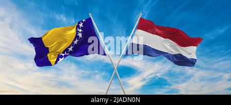 Zwei gekreuzte Flaggen Bosnien und Herzegowina und Niederlande winken im Wind bei bewölktem Himmel. Konzept der Beziehung, des Dialogs, des Reisens zwischen zwei Ländern Stockfoto