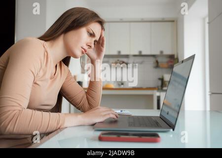 Seitenansicht traurige Frau, die auf den Laptop-Bildschirm mit gelehnt Kopf auf der Hand schaut Stockfoto