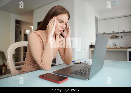 Gestresste junge Frau, die nach der Computerarbeit unter Kopfschmerzen leidet Stockfoto