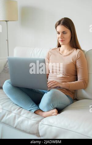 Ganzkörperfoto der jungen Teenager-Frau, die einen Laptop auf dem heimischen Sofa verwendet Stockfoto