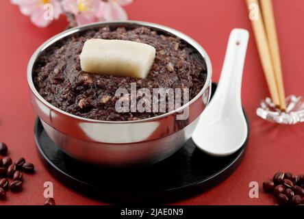 Oshiruko, Zenzai, süße rote Bohnen-Suppe mit Reiskuchen, auf rotem Tisch Stockfoto