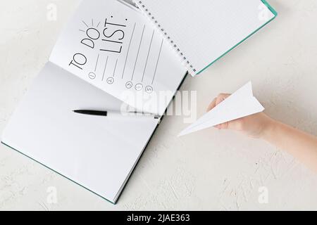 Die Hand des Kindes hält die Papierebene und das Notizbuch mit einer leeren To-Do-Liste auf hellem Hintergrund Stockfoto