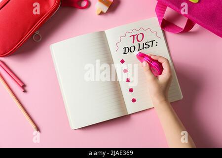 Kinderhand und Notizbuch mit leerer To-Do-Liste auf rosa Hintergrund Stockfoto