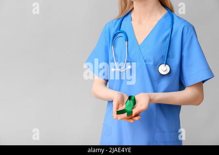 Ärztin mit grünem Band und Stethoskop auf grauem Hintergrund. Leberkrebs-Konzept Stockfoto